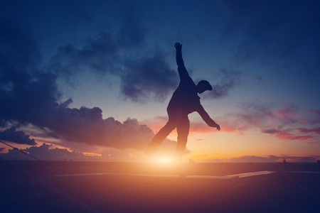 Silhouette of a young active man walking balance on top of the roof in the city at sunset