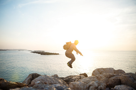 brave man with backpack jumping over rocksの写真素材