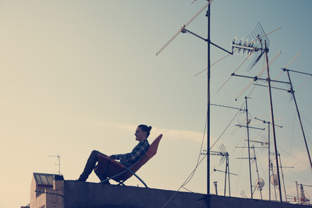 Silhouette of young traveler sitting and resting on the chair on the roof in the cityの写真素材