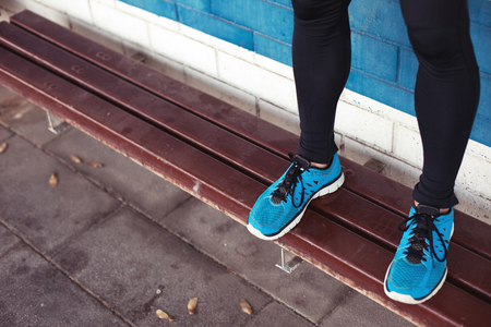 close-up of athlete's legs with blue running shoes standing on benchの写真素材