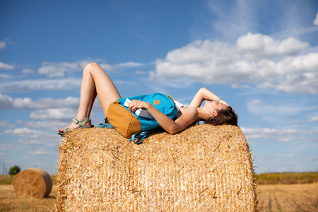 Young and handsome girl resting on haystack with a backpackの写真素材