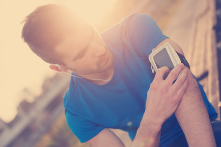 Athlete finding music on mobile phone on his arm (intentional sun glare and vintage color)の写真素材