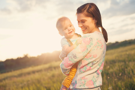 Happy and smiling mother with her baby spending time in the park (intentional sun glare)