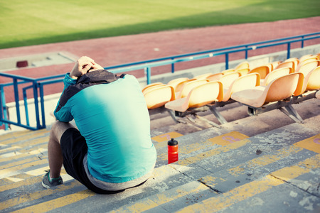 tired athlete after failing resting with a bottle of water sitting on the stairs at stadiumの写真素材