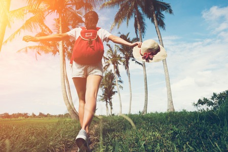 Young and active girl with outspread hands walking at sunny day near palm trees intentional sun glareの写真素材