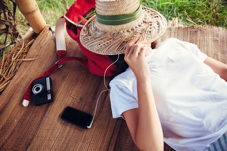 Young girl with straw hat resting outdoors and listening music with headphones at good sunny dayの写真素材