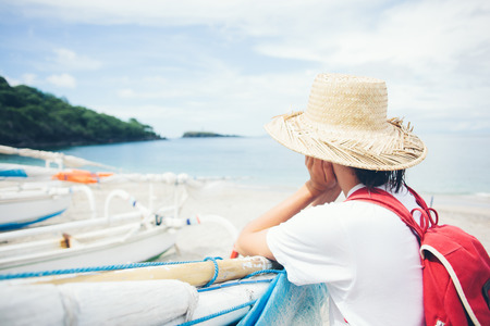 Young woman looking far away standing near sailboats on beautiful islandの写真素材