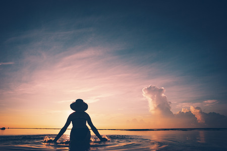 Womans silhouette splashing in water at sunrise