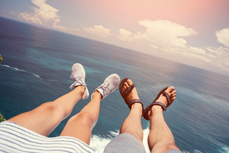 Man in sandals and woman in sport shoes sitting above the oceanの写真素材