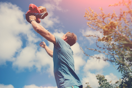 Father playing and catching his daughter in the field outdoors, intentional sun glareの写真素材
