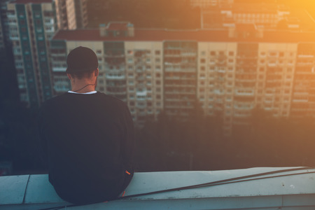 Brave man sitting and chilling on the edge of the roof at sunset, outdoorsの写真素材