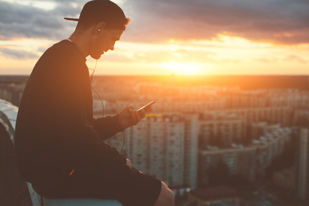 Brave man sitting and chilling on the top of the roof at sunset, outdoorsの写真素材