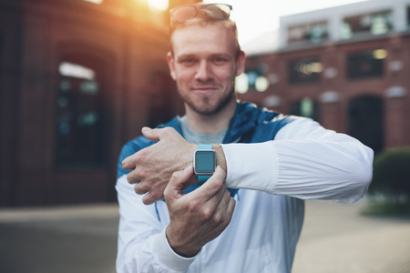 Cheerful man showing his smart watches on the wrist at sunset, outdoorsの写真素材