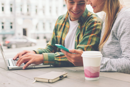 Happy couple having coffee break together and using smartphone, outdoorsの写真素材