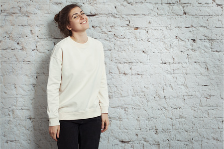 Portrait of cheerful woman hipster wearing blank sweater. White bricks wall background, studio indoorsの写真素材