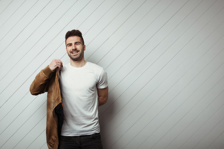 Smiling man in blank t-shirt and jacket, white wooden wall background, studio indoorsの写真素材