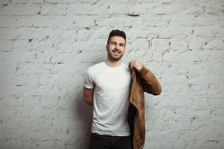 Smiling man in blank t-shirt and jacket, white bricks wall background, studio indoorsの写真素材