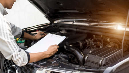 Automobile mechanic repairman checking a car engine with inspecting writing to the clipboard the checklist for repair machine, car service and maintenance.の写真素材