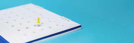 Yellow pin on event calendar. Planner calendar on blue background, plan for business meetings.の写真素材