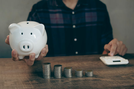 Man putting coin into piggy bank with stack of coins for saving money concept.の写真素材