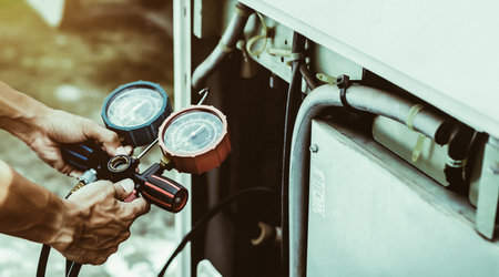 Air repair mechanic using measuring equipment for filling industrial factory air conditioners and checking maintenance outdoor air compressor unit.の写真素材