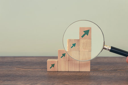 Stacked wooden blocks with green arrows representing growth, progress and success on wooden and grey background.の写真素材