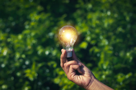 Hand holding light bulb, green leaf background, natural energy concept, inspiration, creativity,...