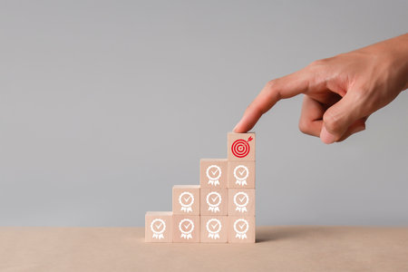 Hand arranging wood block stacking as step stair and target icon on gray background.の写真素材
