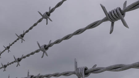 Barbed wire against gray cloudy sky