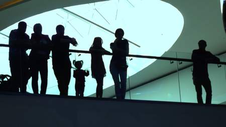 Silhouettes of adults and kids standing near glassy handrail in modern buildingの写真素材