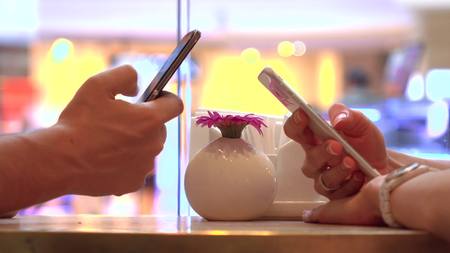 Girl and man tapping their mobile phone touchscreens in a cafe. Modern mobile phone addiction