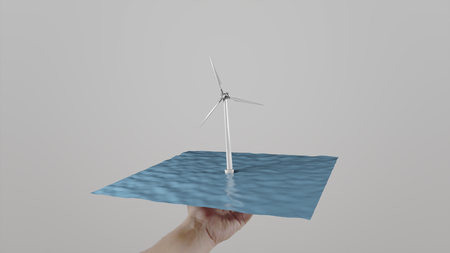 Man twists in hand a windmill located on water. Gray background. Alternative ecologic power generationの写真素材