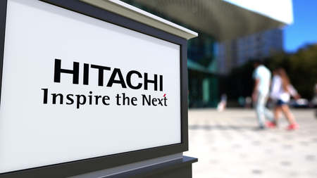 Street signage board with Hitachi logo. Blurred office center and walking people background. Editorial 3D rendering United Statesのeditorial素材