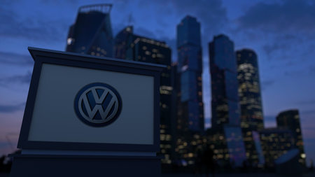Street signage board with Volkswagen logo in the evening. Blurred business district skyscrapers background. Editorial 3D United Statesのeditorial素材