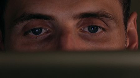 Grey eyes of focused young man using his tablet computer. Screen reflecting in the eyes, device lighting glowの写真素材