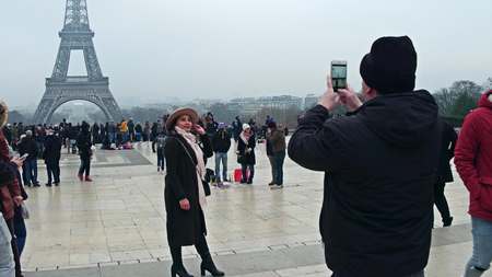 PARIS, FRANCE - DECEMBER, 31, 2016. Beautiful young woman wearing hat poses near Eiffel Tower on a foggy day. The most popular French landmark and touristic destinationのeditorial素材