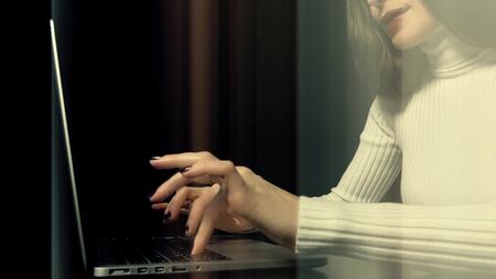 Beautiful brunette woman working on her laptop against black background. Abstract light vertical lines across the frameの写真素材