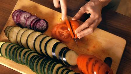 Young woman slicing juicy red tomato. Cooking homemade ratatouilleの写真素材
