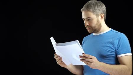 Handsome man in blue tshirt looking through papers. Cotract, bills, letter concepts. Black...