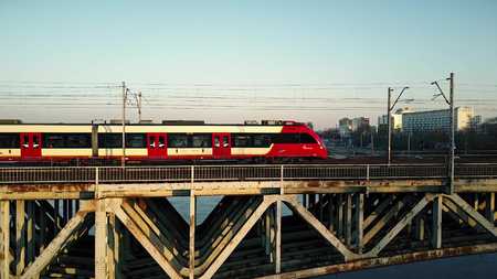 WARSAW, POLAND - MARCH, 27, 2017. Aerial shot of red passenger train moving on railway bridge across the riverのeditorial素材