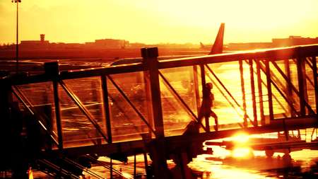 Silhouette of a young woman walking in a glass jet bridge. Boarding a plane at the airport in the eveningの写真素材
