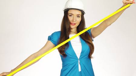Beautiful female construction engineer or architect in hard hat using measure tape against white backgroundの写真素材