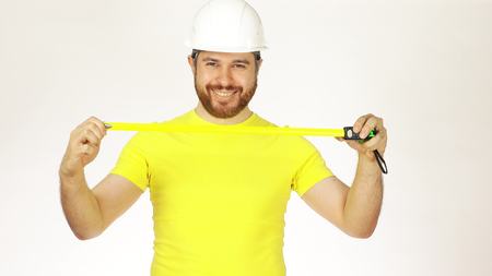 Cheerful construction engineer or architect in yellow tshirt and hard hat using measure tape against white backgroundの写真素材