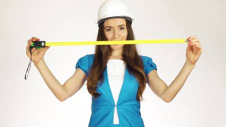 Beautiful female construction engineer or architect using measure tape against white background