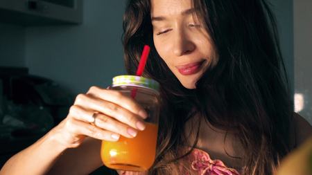 Beautiful young woman drinking fresh orange juice at homeの写真素材