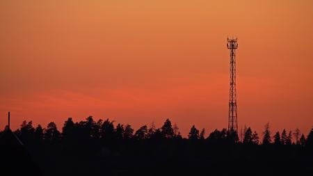 Silhouette of a cell tower against orange sunset skyの写真素材