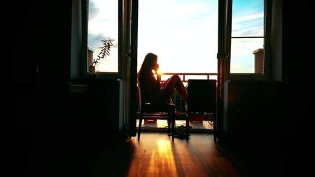 Silhouette of a beautiful girl talking on her cellphone at homeの写真素材
