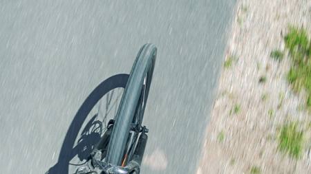 Blurred asphalt road and spinning bicycle front wheel and fork, top down view