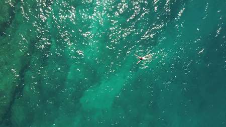Aerial top down view of a girl in a white swimsuit swimming in the seaの写真素材