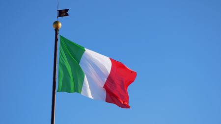 Waving big Italian flag against blue cloudless skyの写真素材
